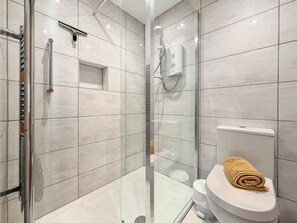 A modern bathroom with a glass-enclosed shower, a toilet with a towel, and a small shelf. - 3 bedroom accommodation in Christchurch (Christchurch)