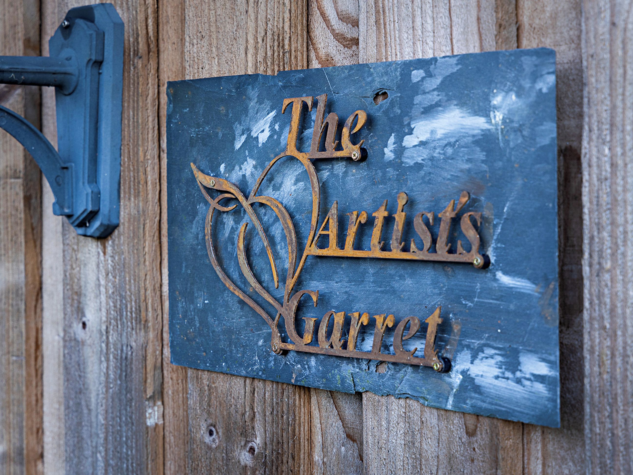 A metal sign with the inscription 'The Artist's Garret' mounted on a wooden surface.