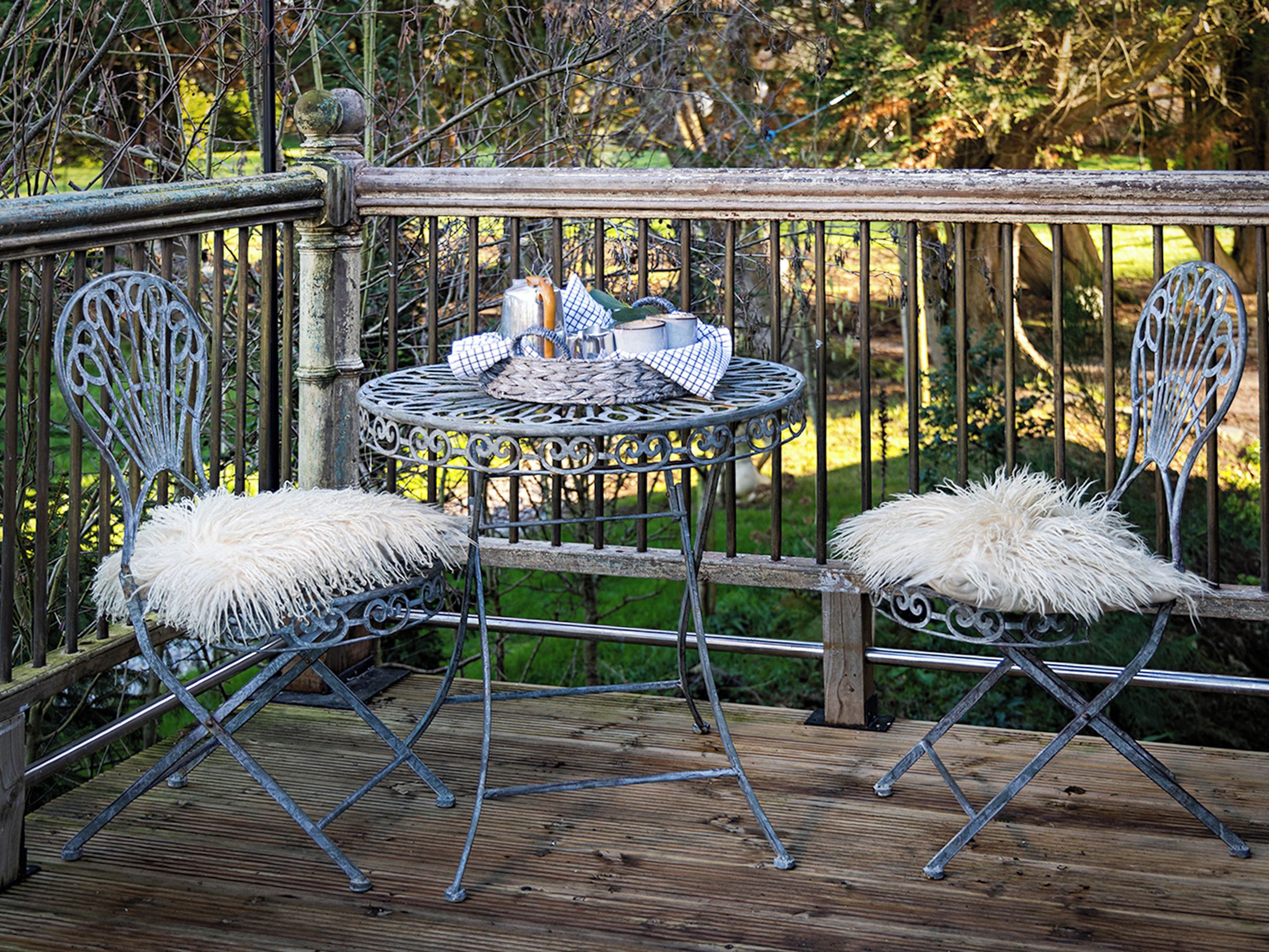 Une table en métal, entourée de chaises, est posée sur une terrasse en bois, elle-même délimitée par une rambarde en bois.