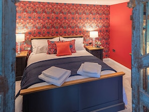 Une chambre à coucher avec un lit, deux tables de chevet, une commode et un papier peint à motifs.