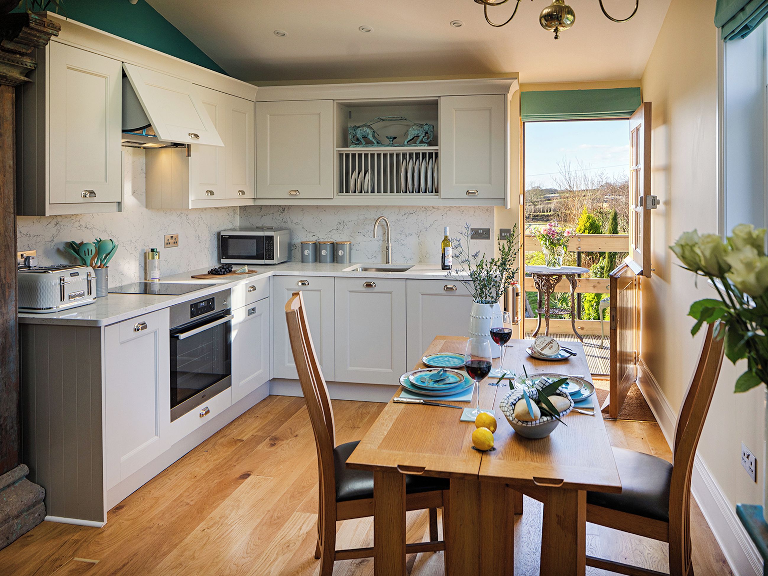 A modern kitchen with white cabinetry, a dining table set for two, and a view of the outdoors.