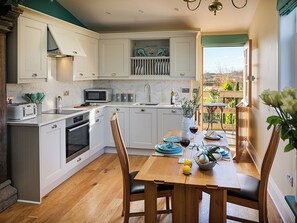 Une cuisine moderne avec des meubles blancs, une table à manger dressée pour deux personnes et une vue sur l’extérieur.