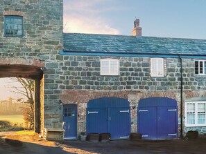 A stone building with a blue roof, three blue doors, and a chimney. - Coach House - UKC9986 (Llanfairpwllgwyngyll)