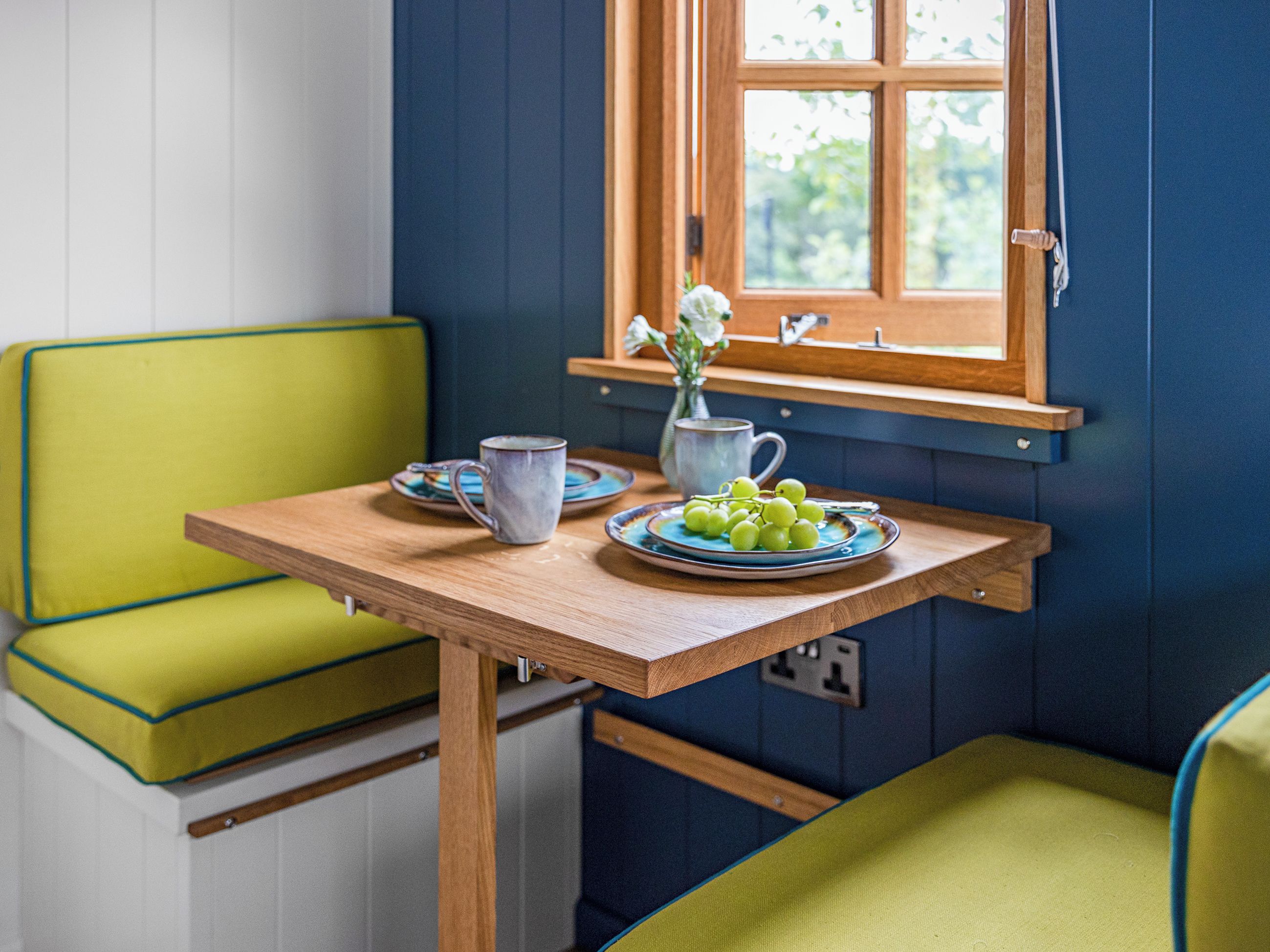 A small room with a wooden table, a green chair, and a window with a view of greenery.