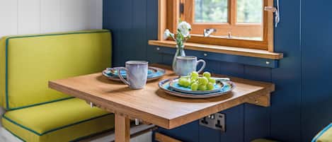 A small room with a wooden table, a green chair, and a window with a view of greenery.