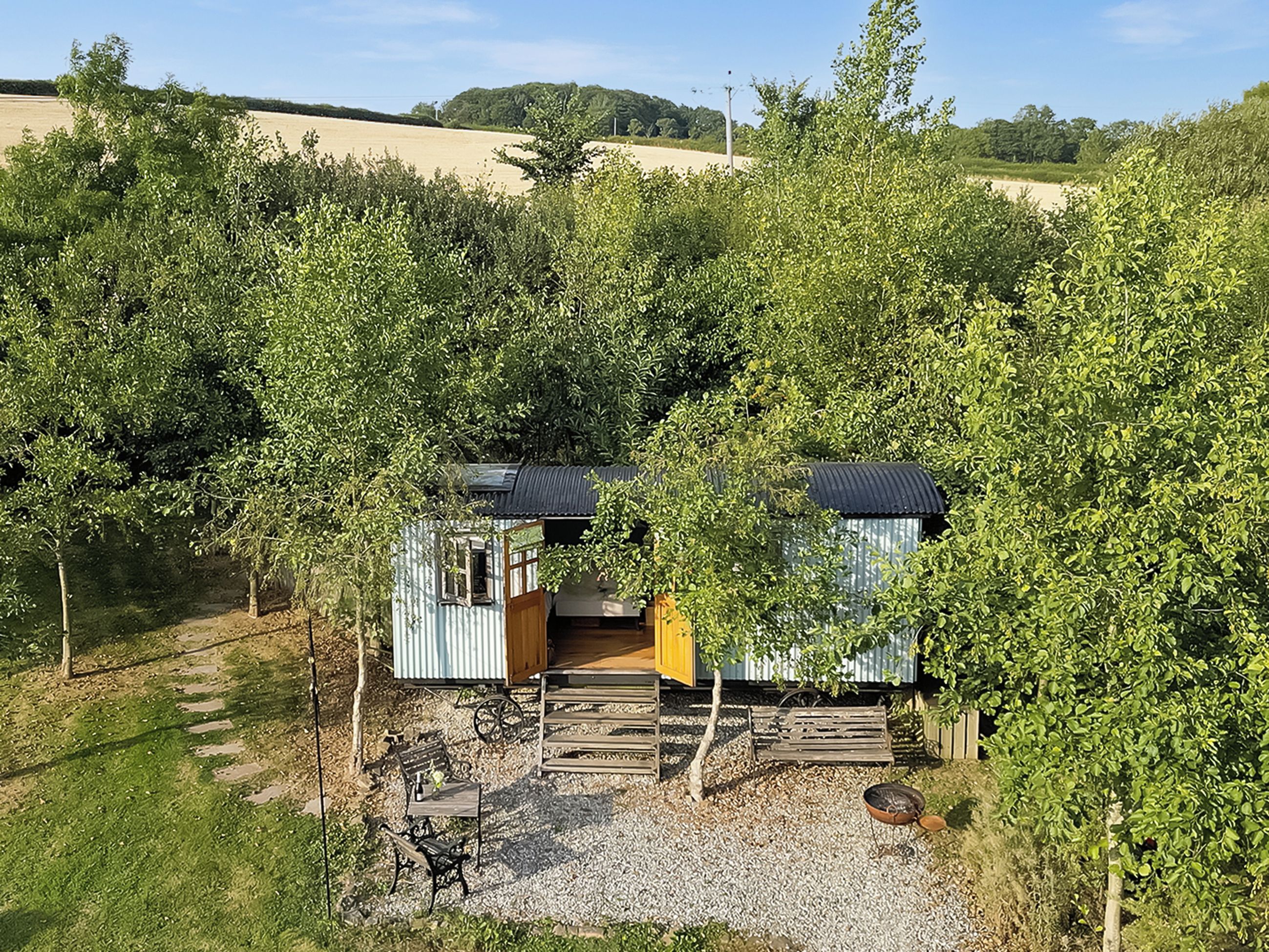 A small, rustic cabin with a wooden deck and a gravel path leading to it, surrounded by dense greenery.