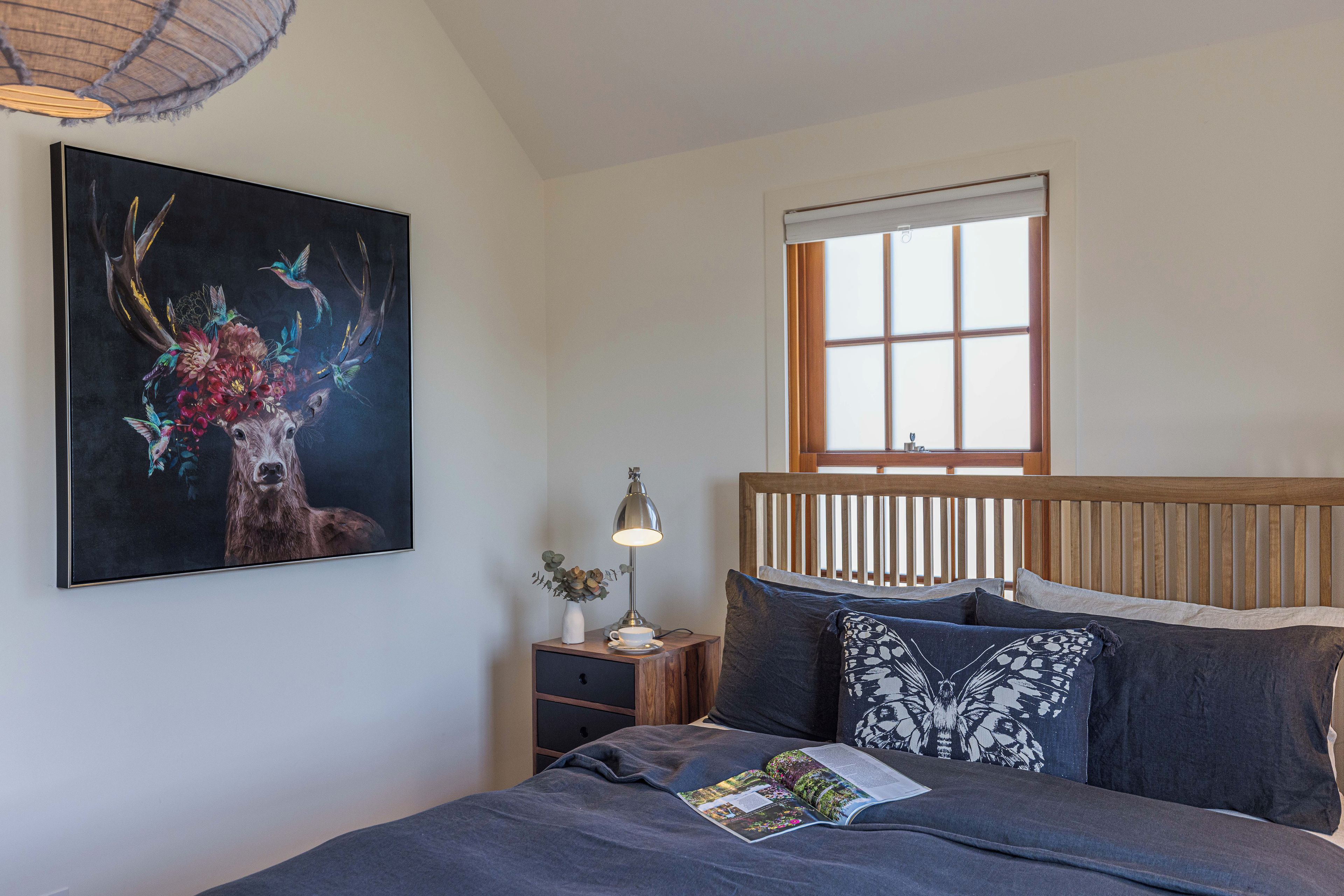 Ein Schlafzimmer mit Bett, Nachttisch, Lampe, Fenster und einem Bild an der Wand.