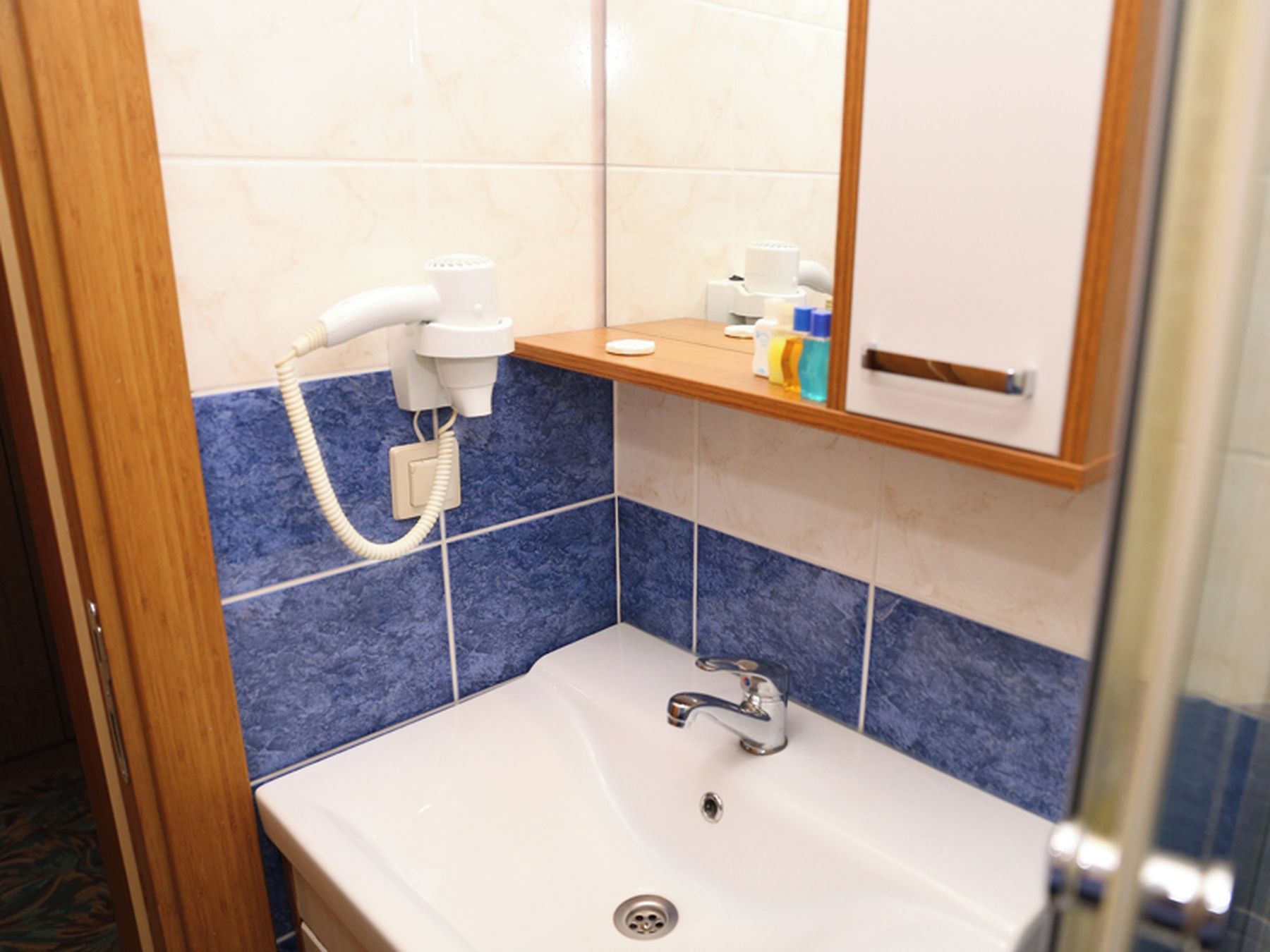 A bathroom with a white sink, blue-tiled walls, a mirror, and a hairdryer on a shelf.