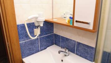 A bathroom with a white sink, blue-tiled walls, a mirror, and a hairdryer on a shelf.