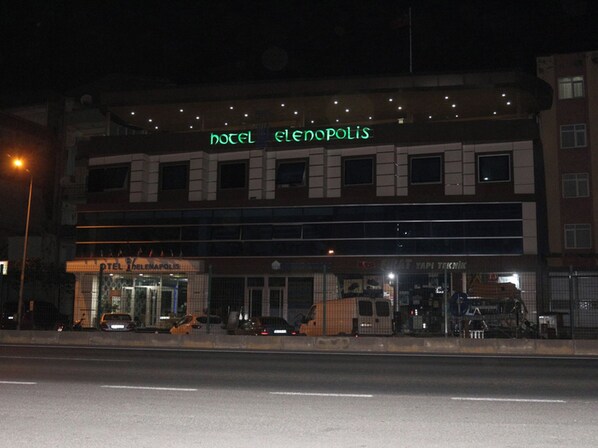 Un hotel con un letrero de neón, entrada de vidrio y coches estacionados al frente.
