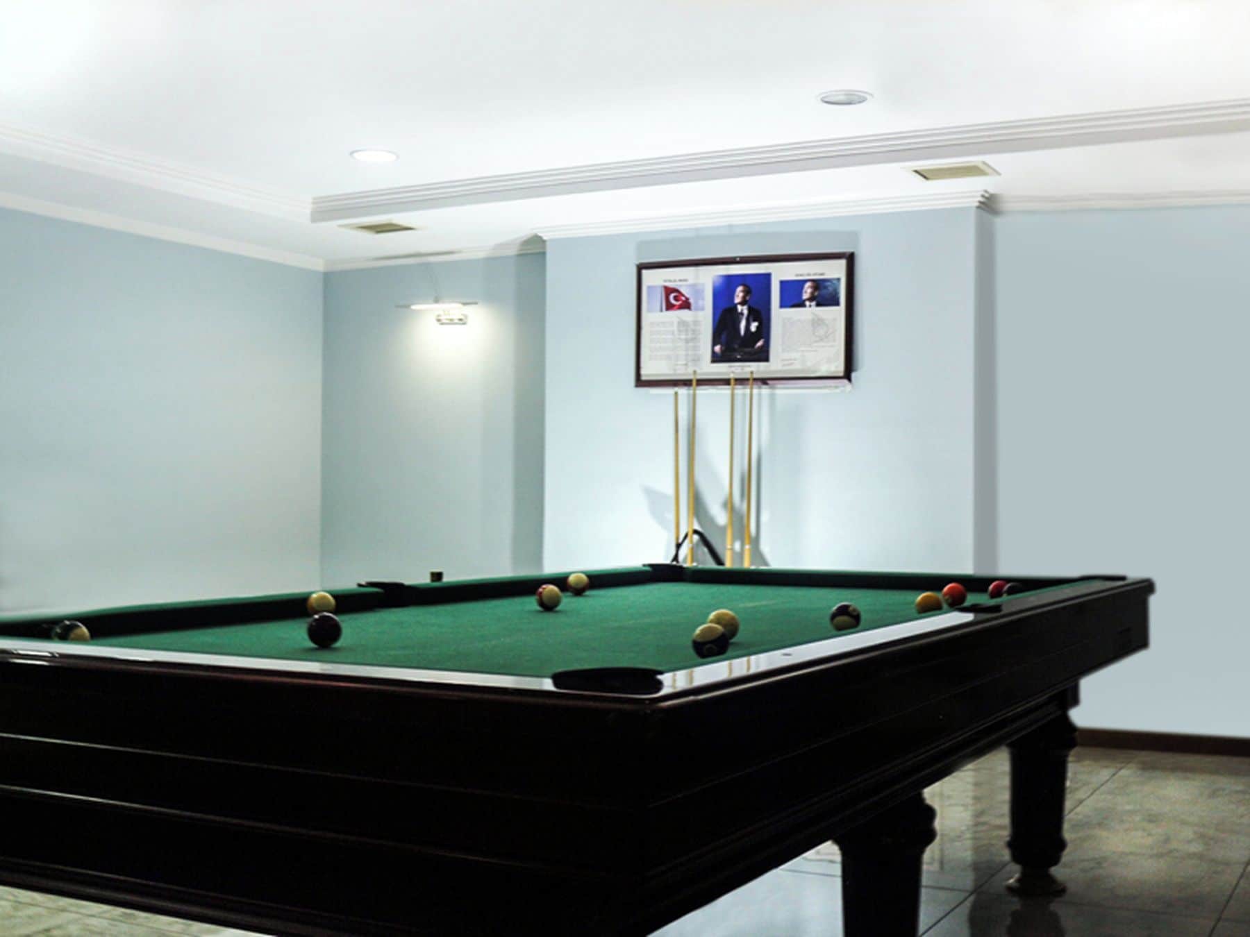 Una mesa de billar con bolas, un televisor montado en la pared y una lámpara en el techo.