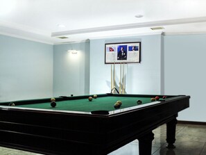 Una mesa de billar con bolas, un televisor montado en la pared y una lámpara en el techo.