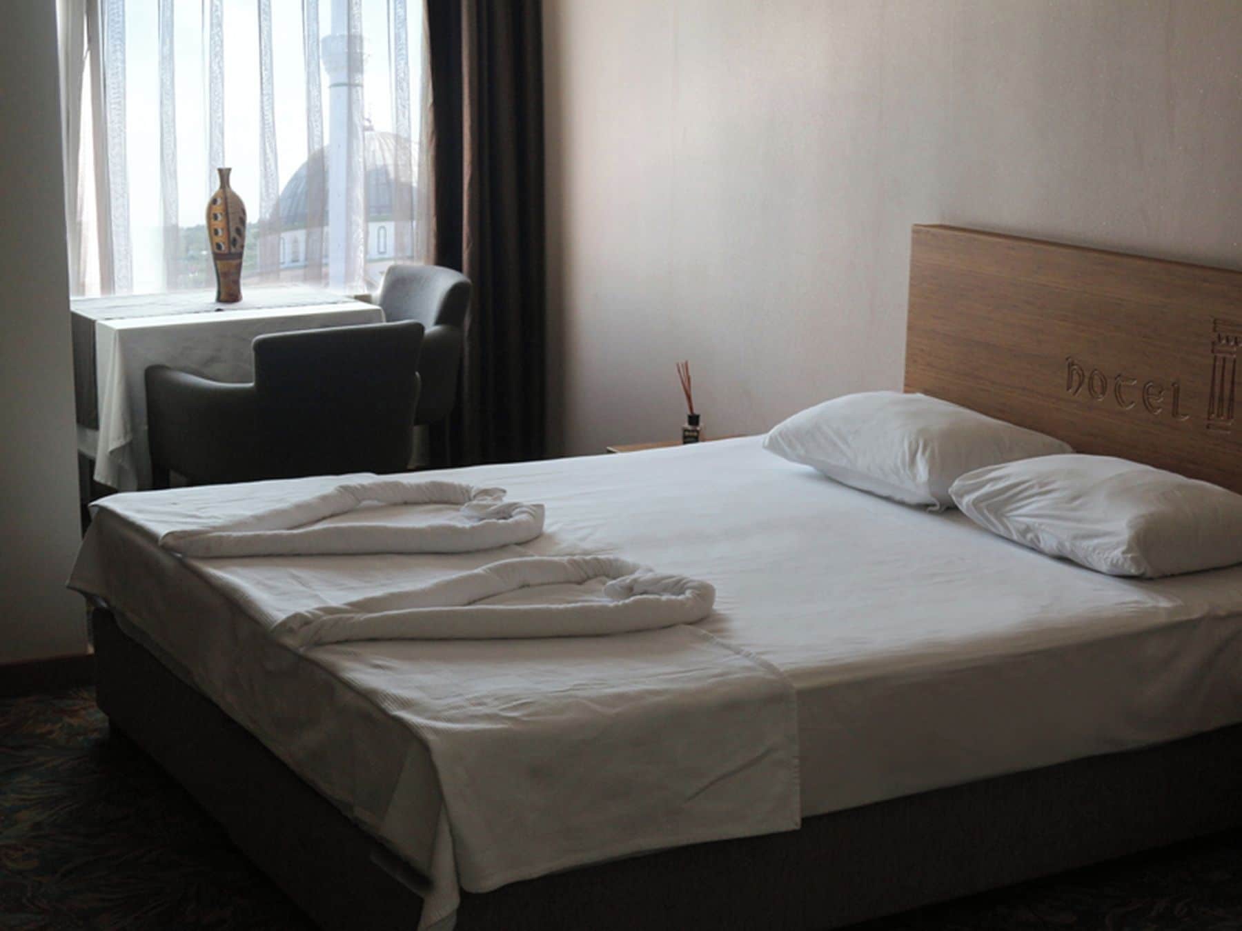 Habitación de hotel con cama, una silla, una mesa y ventana con vista a un edificio.