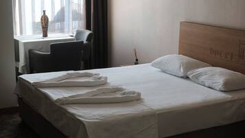 Habitación de hotel con cama, una silla, una mesa y ventana con vista a un edificio.
