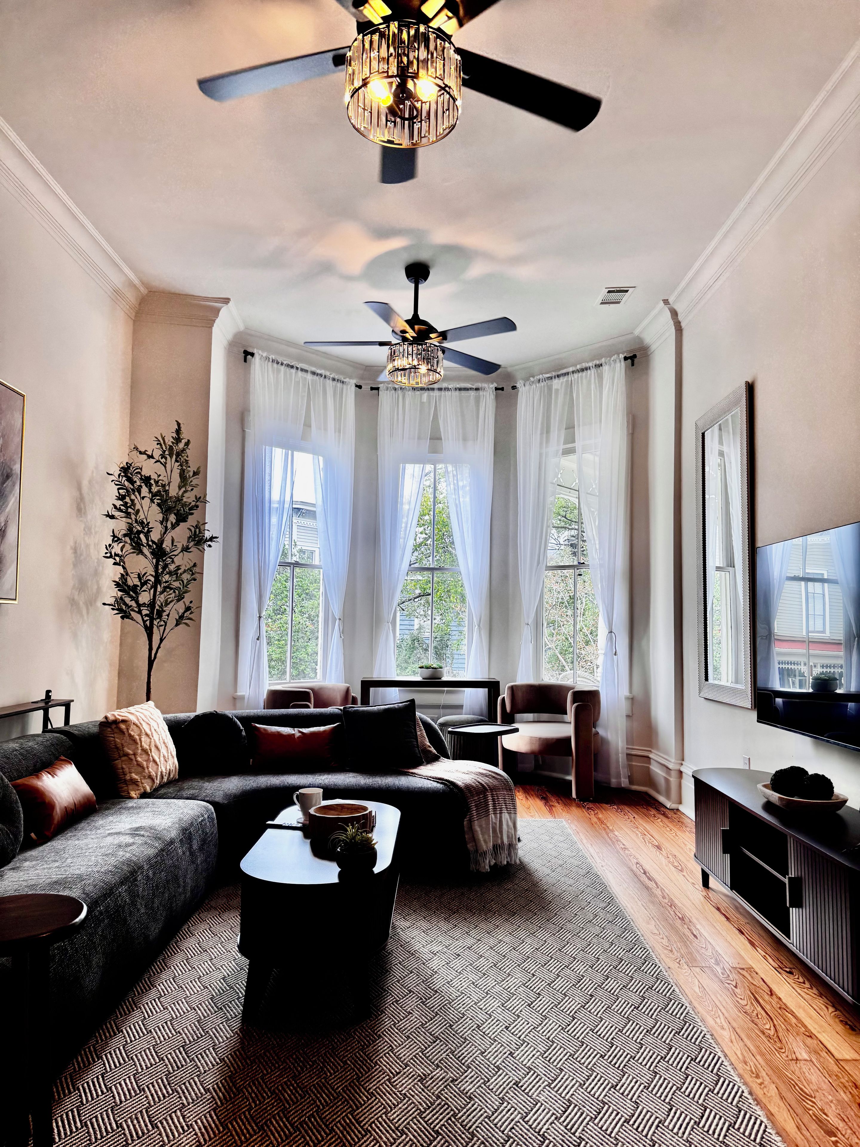 A modern living room with a sectional sofa, a coffee table, a television, and a ceiling fan.