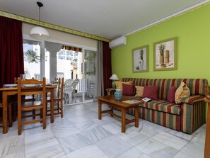 A living room with a sofa, a dining table with chairs, a coffee table, and a view of the outside. - Sunstay Relax 48 Rio Marina Nerja (Nerja)