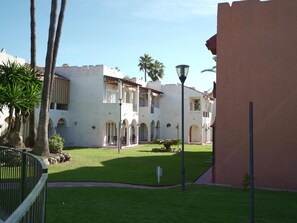 Une cour avec un bâtiment blanc, des palmiers et un lampadaire.