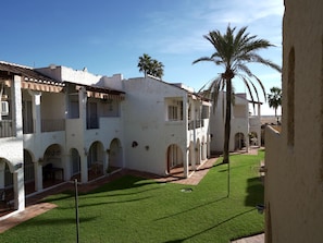 A courtyard with white buildings, palm trees, and a green lawn. - Sunstay Relax 48 Rio Marina Nerja (Nerja)