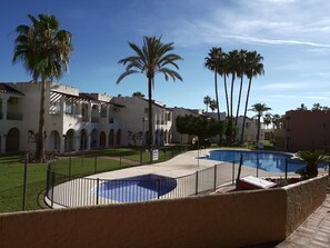 A pool area with a palm tree, a building with arched windows, and a clear blue sky. - Sunstay Relax 48 Rio Marina Nerja (Nerja)
