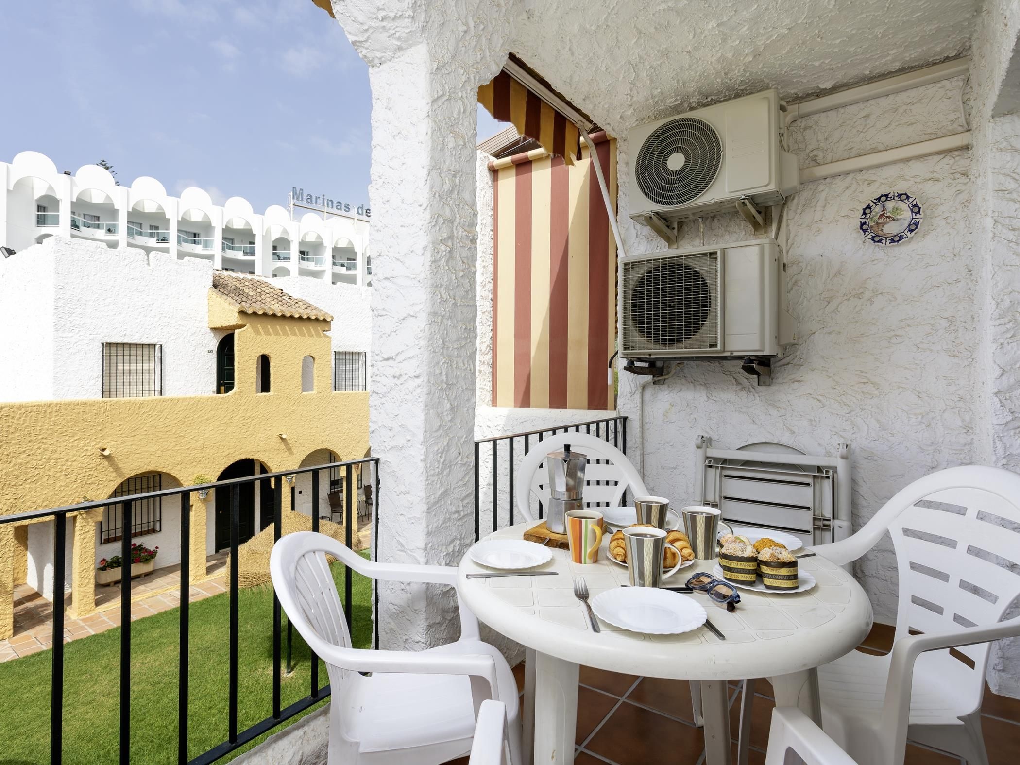 Un balcon avec des chaises blanches, une table avec des aliments pour le petit-déjeuner et un appareil de climatisation.