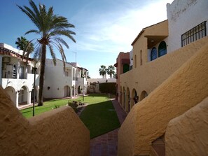 A courtyard with a palm tree, a pathway, and buildings with arches and balconies. - Sunstay Relax 48 Rio Marina Nerja (Nerja)