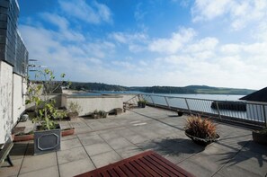 Una terraza en la azotea con vistas al mar, plantas en macetas y un banco de madera.