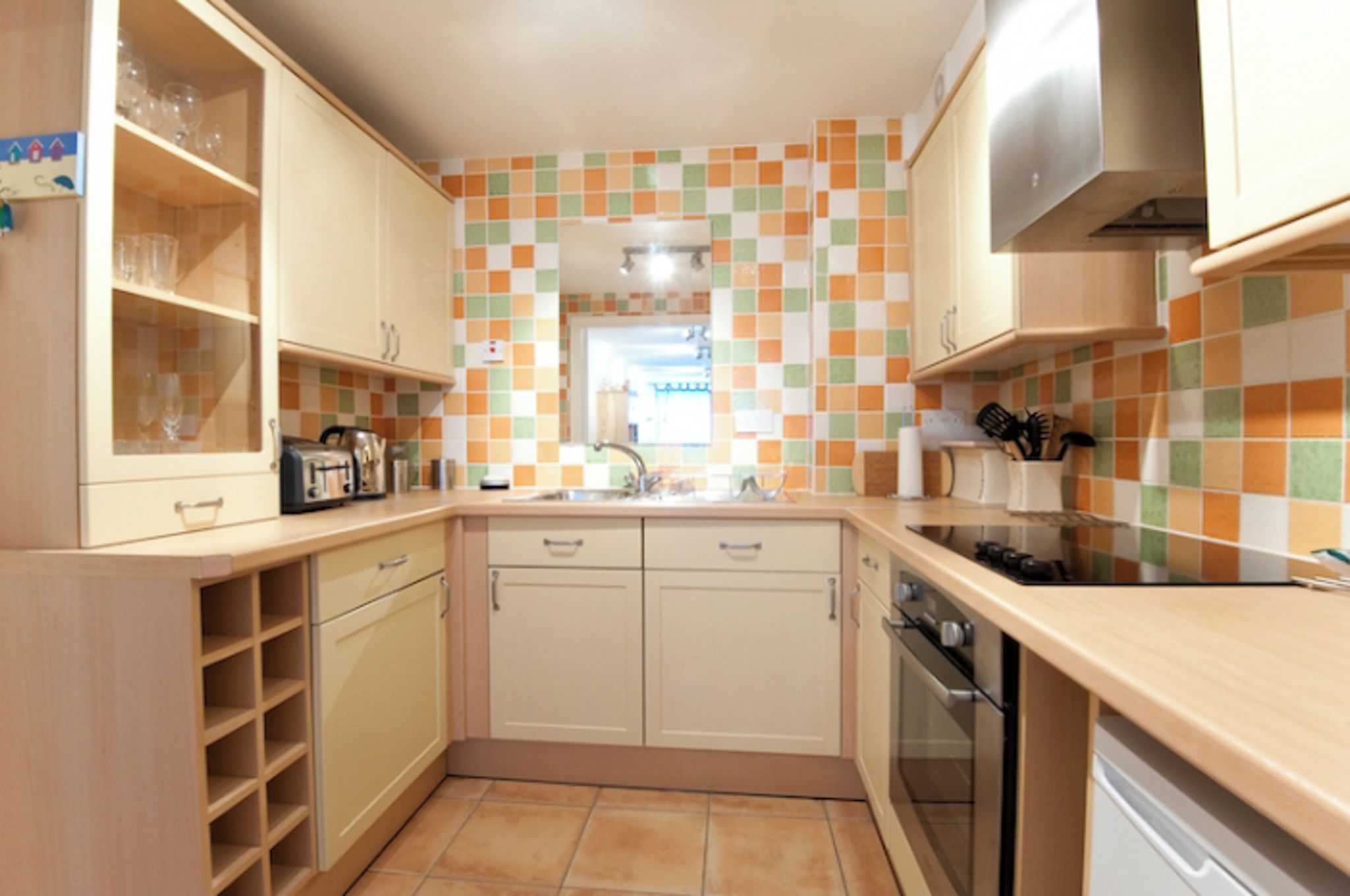 Una cocina con armarios de colores claros, un salpicadero de azulejos, una estufa y un fregadero.