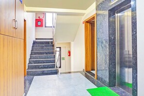 Un hall d’hôtel avec un escalier en marbre, des portes en bois et un ascenseur.