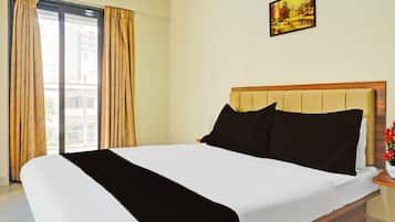 A hotel room with a bed, a painting on the wall, and a window with curtains.