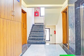 Corredor de hotel com escadaria de mármore, portas de madeira e extintor de incêndio na parede.