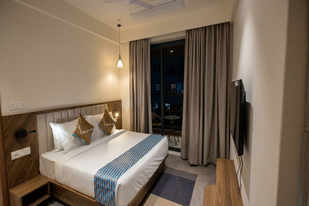 A hotel room with a bed, a TV, a window with curtains, and a ceiling fan.