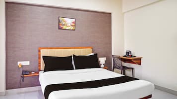 A hotel room with a bed, bedside table, lamp, and a small desk with a chair.