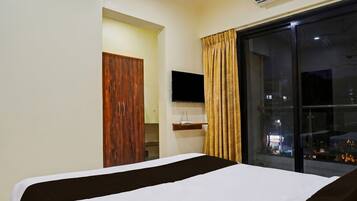 A hotel room with a bed, a TV, a window with curtains, and an air conditioning unit.