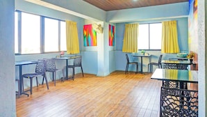 A room with a wooden floor, two windows with yellow curtains, a table with chairs, and a ceiling fan. - Super Townhouse Hitech City Near Yashoda (Hyderabad)
