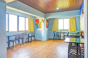 A room with a wooden floor, two windows with yellow curtains, a table with chairs, and a ceiling fan. - Super Townhouse Hitech City Near Yashoda (Hyderabad)