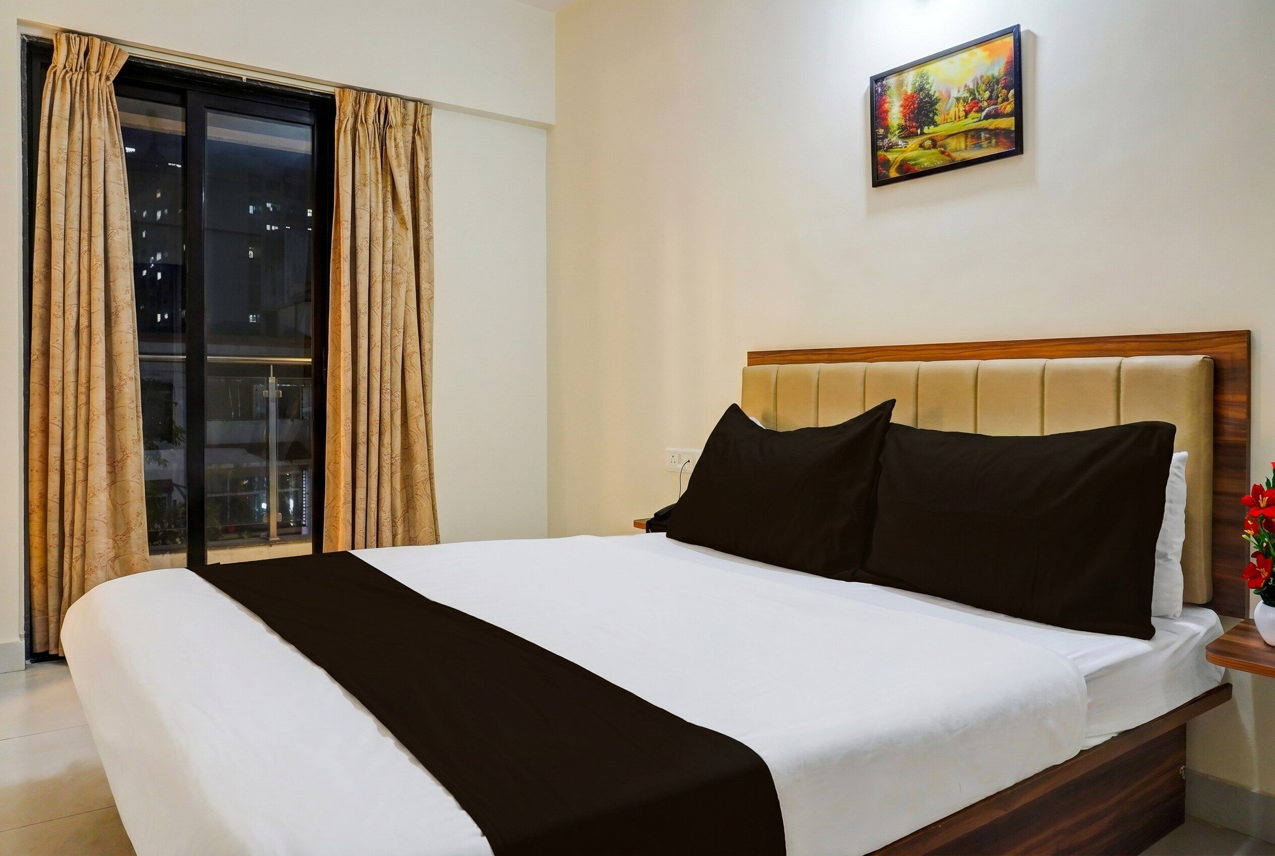 Ein Hotelzimmer mit Bett, Nachttisch, einem Bild an der Wand und Blick durch das Fenster.