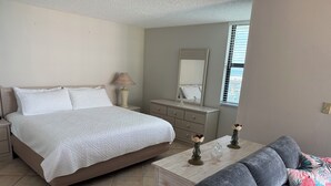 Een slaapkamer met een bed, nachtkastjes, een dressoir, een spiegel en een raam met jaloezieën.