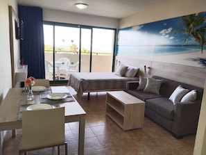 Ein Hotelzimmer mit Bett, Sofa, Esstisch mit Stühlen und einem Balkon mit Aussicht.