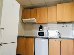 Eine kompakte Küche mit Holzschränken, einem weißen Kühlschrank, einer Mikrowelle, einer Kaffeemaschine und einem Geschirrspüler.