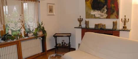 Een woonkamer met een witte bank, een radiator, een tafel met een glazen schaal, en een schilderij aan de muur.