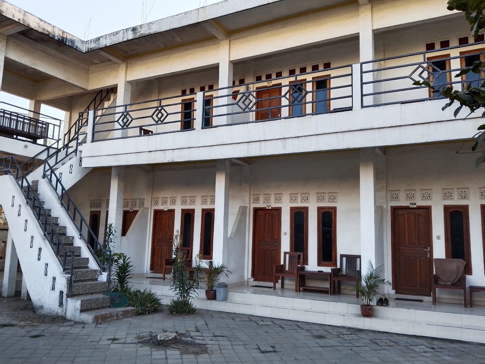A multi-story building with a staircase, wooden doors, and a balcony with railings.