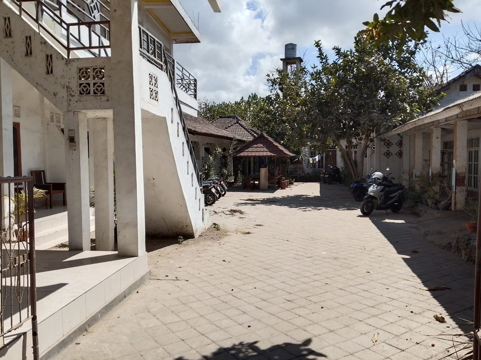 A paved courtyard with a gazebo, a water tank, and parked motorcycles.
