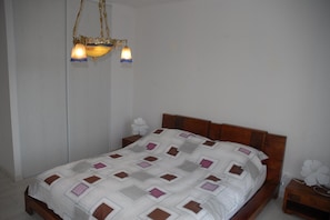 Ein Schlafzimmer mit einem hölzernen Bett, einer weißen Wand und einer Pendelleuchte.