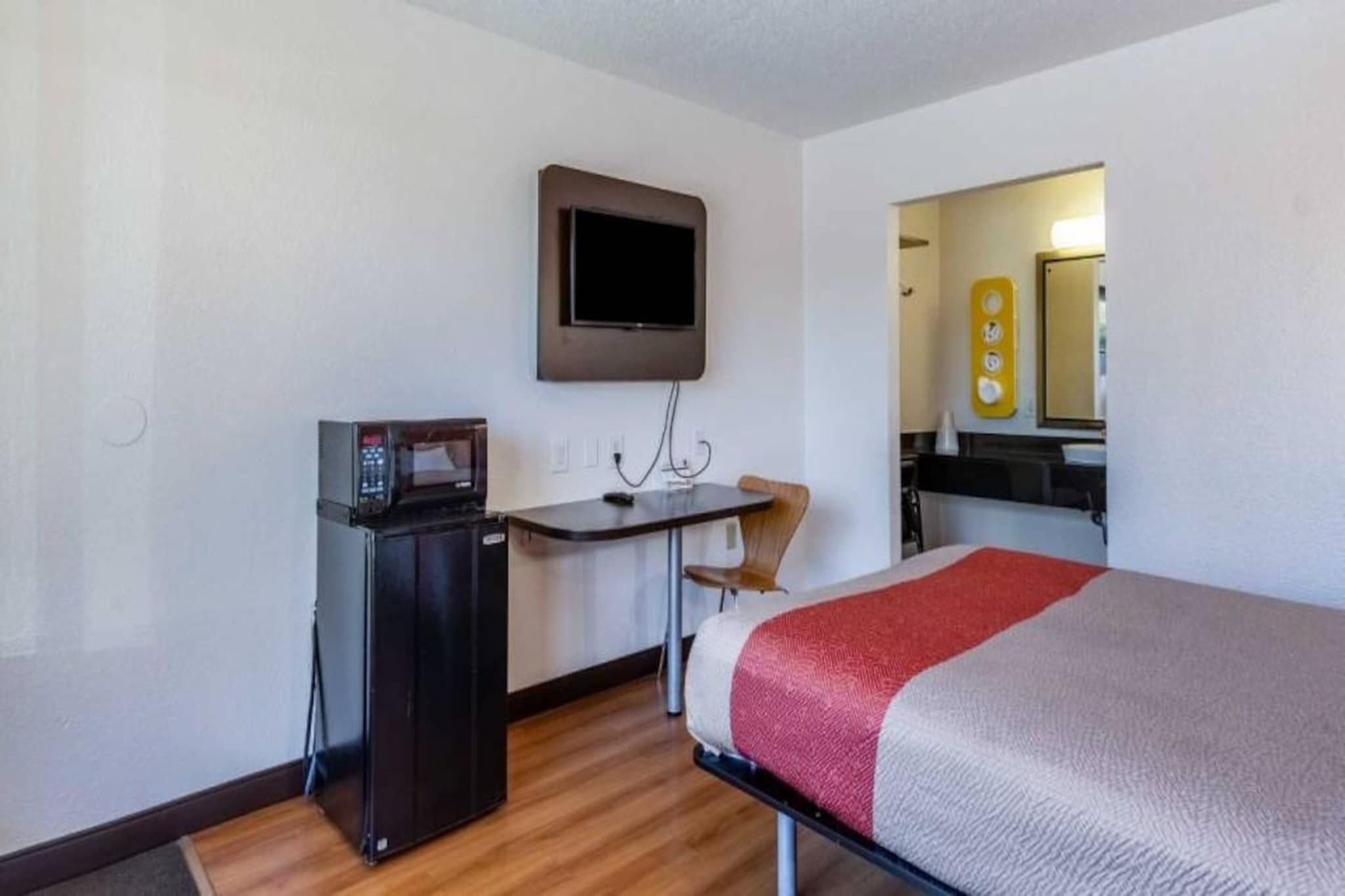 A hotel room with a bed, a desk, a television mounted on the wall, and a kitchenette area.