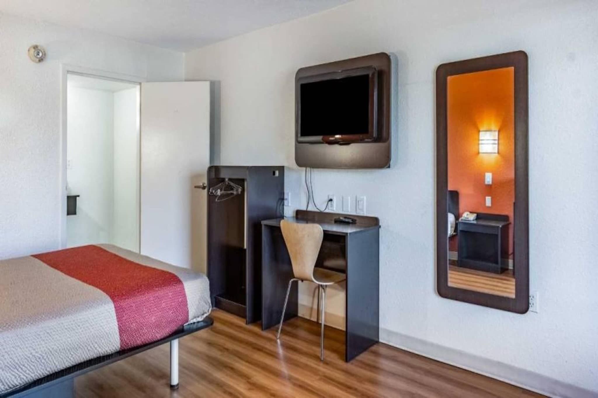 A hotel room with a bed, a desk, a chair, a television, and a mirror.