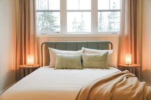 A bed with a headboard, two bedside lamps, and a window with curtains. - Beautiful Muskoka Cottage with Games, BBQ & Views (Huntsville)
