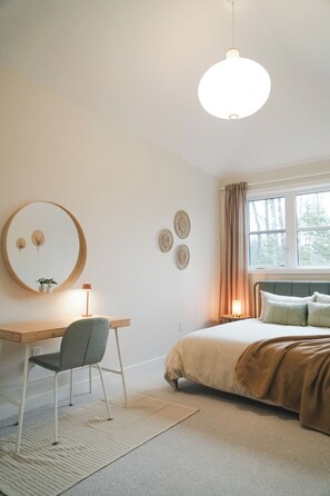 A bedroom with a bed, a desk, a chair, a mirror, and a window with curtains. - Beautiful Muskoka Cottage with Games, BBQ & Views (Huntsville)