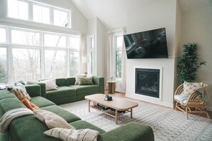 A living room with a green sofa, a coffee table, a flat-screen TV mounted on the wall, and a fireplace. - Beautiful Muskoka Cottage with Games, BBQ & Views (Huntsville)