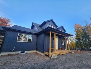 A two-story house with a dark blue exterior, a front porch with wooden steps, and a gravel driveway. - Beautiful Muskoka Cottage with Games, BBQ & Views (Huntsville)