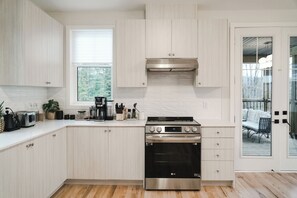 A modern kitchen with light wood cabinets, a stainless steel range, and a window with a view of trees. - Beautiful Muskoka Cottage with Games, BBQ & Views (Huntsville)